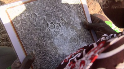 Ningura Napurrula hält das Bild &quot;Papunya, Felsloch im Westen von Kintore&quot; (in einer Verkleinerung) in ihrer Hand.